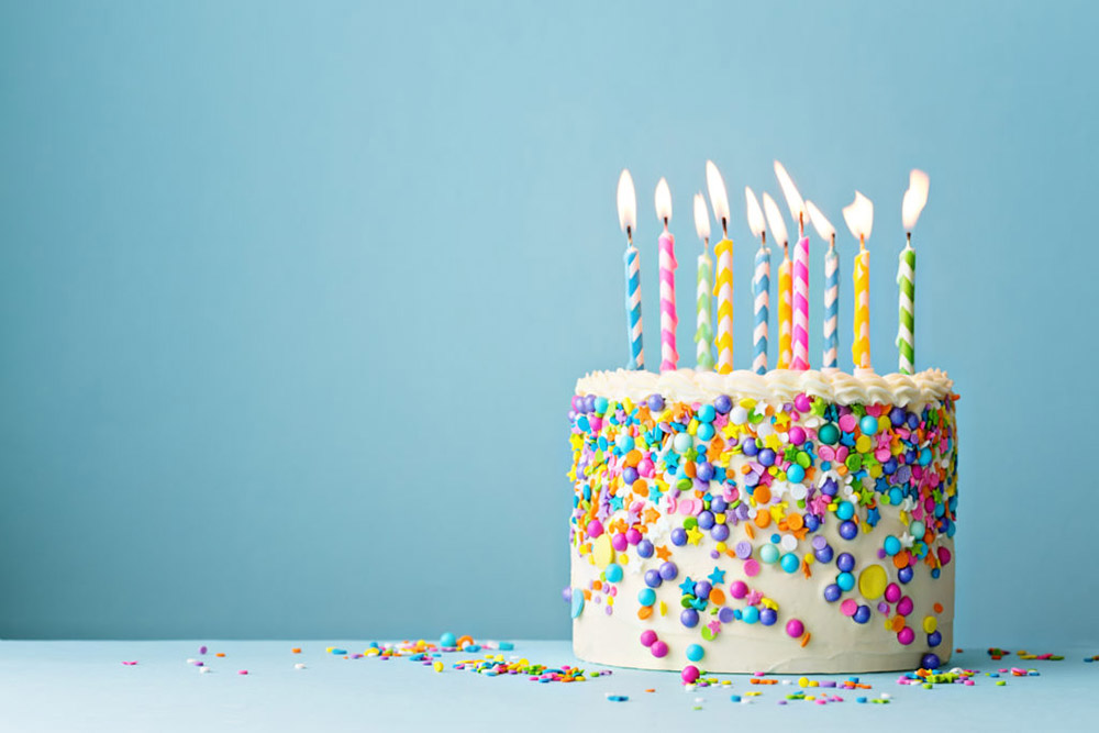 Colorful birthday cake with sprinkles and ten candles on a blue background